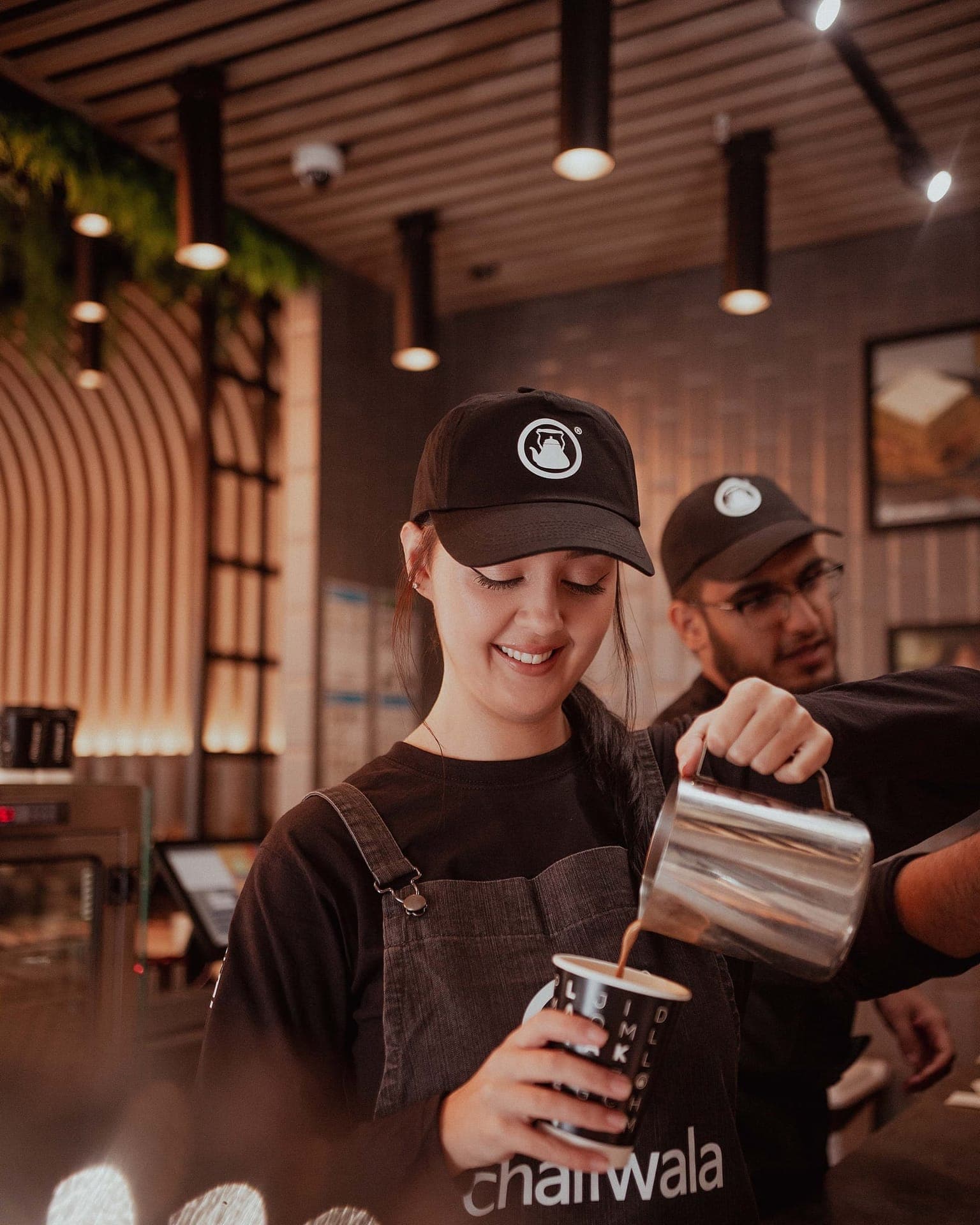 a chaiiwala barista pouring karak chaii into a branded cup