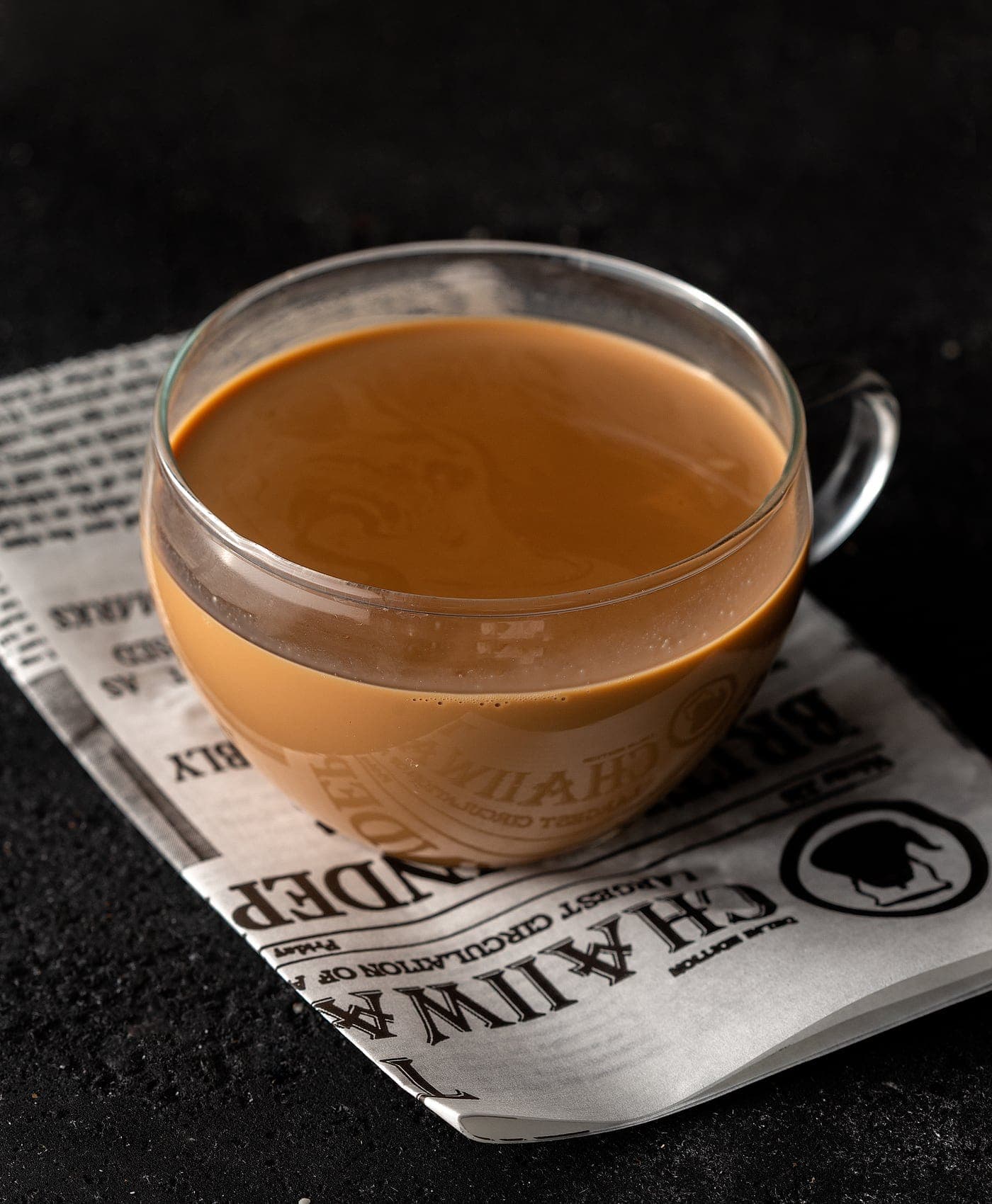 A glass cup of Karak Chaii on a chaiiwala newsprint-lined saucer